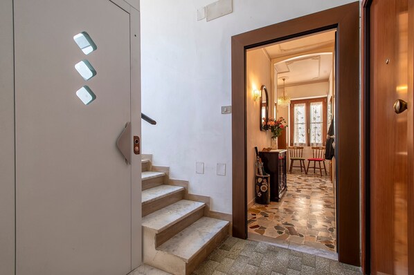 A staircase leading to a room with a wooden door, a tiled floor, and a view into a dining area with chairs and a table.