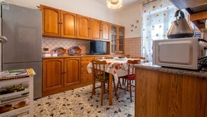 Eine Küche mit Holzschränken, einem Kühlschrank, einer Mikrowelle, einem Esstisch mit Stühlen und einem Fliesenboden.