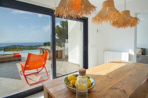 A wooden table with a bowl of lemons and a bottle, a red chair, and a view through a glass door to the outside. - Villa 'Bel Horizonte' with Sea View, Wi-Fi and Air Conditioning (Benissa)
