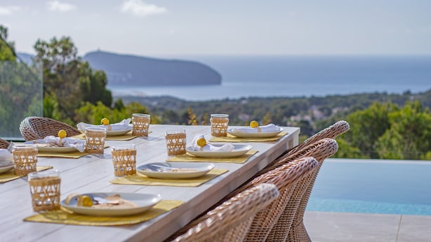 A dining table set with plates, glasses, and napkins, overlooking a pool and ocean view.