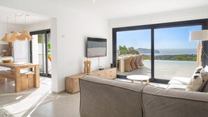 A modern living room with a large sofa, a dining area with a table and chairs, and a TV mounted on the wall.