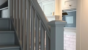 A staircase with a white balustrade leading to a kitchen area with white cabinetry and a built-in oven.
