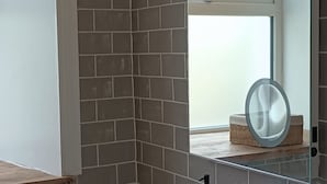 A bathroom with a tiled wall, a window with a view, and a mirror on a glass shelf.