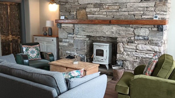 A cozy living room with a stone fireplace, a sofa, a green armchair, and a wooden coffee table.