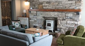 Una sala de estar acogedora con una chimenea de piedra, un sofá, un sillón verde y una mesa de centro de madera.