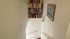 Una escalera conduce a una habitación con una estantería, un cuadro enmarcado y una mesita.