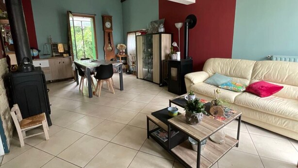 Una sala de estar con sofá, mesa de centro, mesa de comedor con sillas, chimenea y ventana.