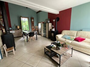 A living room with a sofa, a coffee table, a dining table with chairs, a fireplace, and a window. - Holiday Home in Pradines with Renovated Private Garden (Pradines)