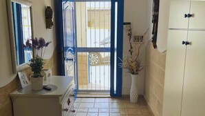 Un pasillo con un armario blanco, un espejo con marco azul, un jarrón con plantas secas y una alfombra estampada.