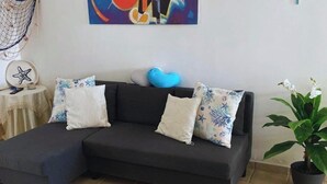 Un sofá de color oscuro con cojines estampados, un objeto en forma de corazón azul y una decoración de estrella de mar sobre una mesita.