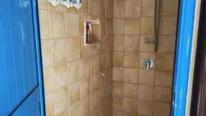 Un espacio de ducha pequeño, con azulejos, una regadera y un estante con artículos de tocador.