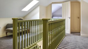 Une pièce avec un plafond en pente, un escalier en bois doté d’une rampe verte, un lit et une porte.