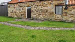 Un bâtiment en pierre avec un toit recouvert de tuiles, une porte et deux petites tables.