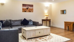 Un salon avec un canapé en cuir, une table basse en bois, un tapis, une lampe et un tableau au mur.