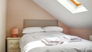 Une chambre avec un plafond en pente, un lit avec une literie blanche, une lampe de chevet et un puits de lumière.