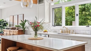 A modern kitchen with a large island, white cabinetry, and a view of greenery outside. - Luxe Lakefront: Spa, Kayaks, Pickleball, & Theater (Macon)