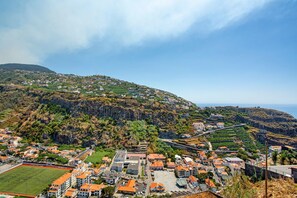 A coastal town with residential buildings, a sports field, and a winding road. - Holiday Home 'Pico The Best View' with Sea View, Private Terrace & Balcony (Ribeira Brava)