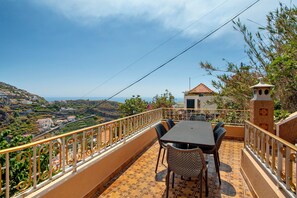 A terrace with a table and chairs, overlooking a scenic landscape with buildings and hills.