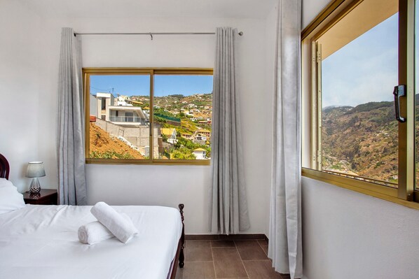 A hotel room with a large window, a bed, a nightstand, and a lamp.