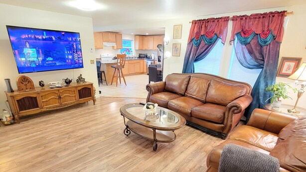 A spacious living room with a leather sofa, a coffee table, and a flat-screen TV mounted on the wall.