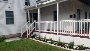 A white two-story house with a covered porch and a small garden with flowers.