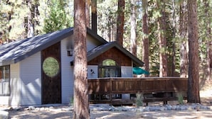 A cabin with a wooden deck, surrounded by tall pine trees.