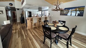 A modern kitchen with a central island, wooden flooring, and a dining area with a round table and chairs.