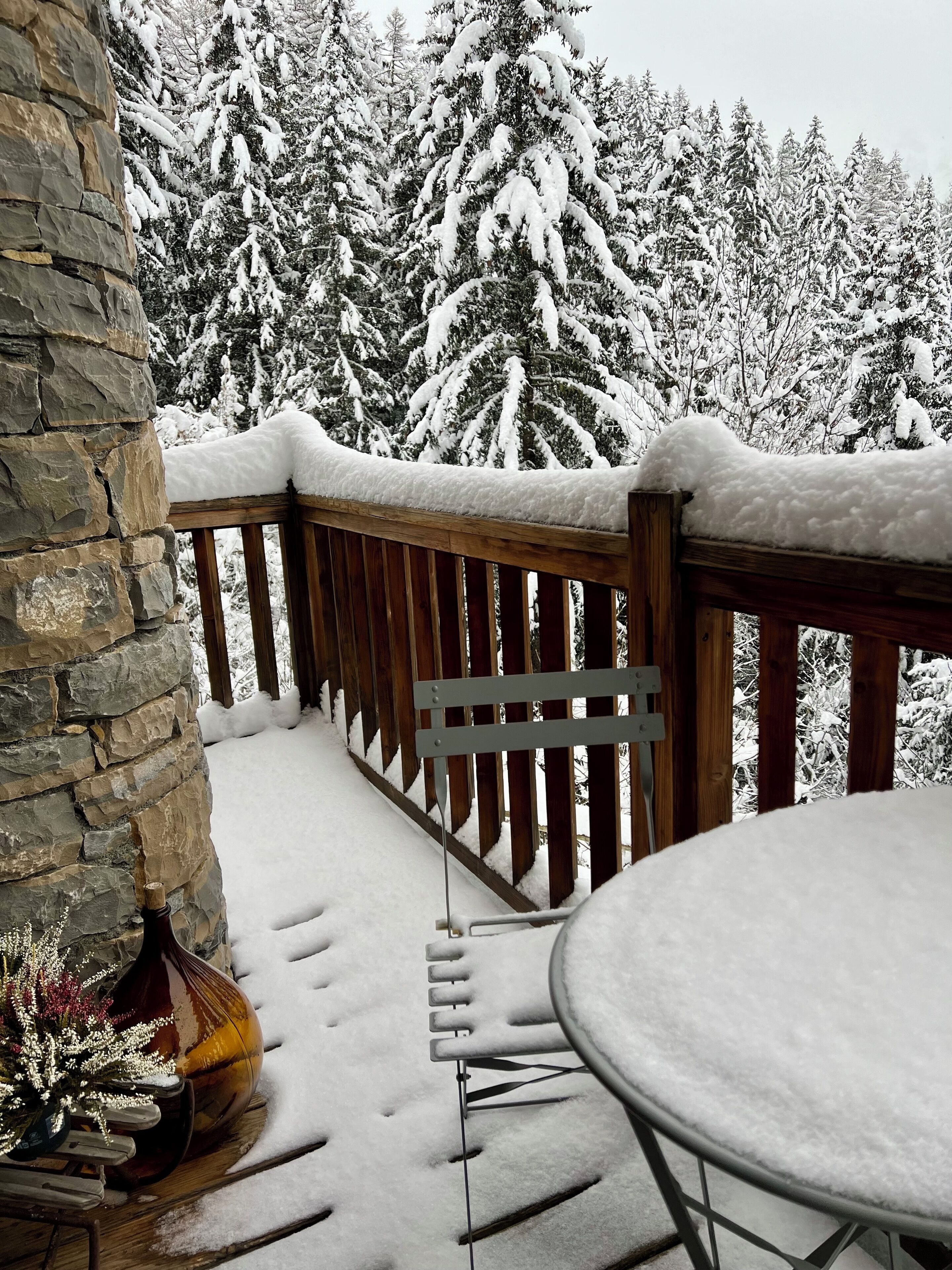 Een sneeuwbedekt terras met een stenen muur en een houten leuning.