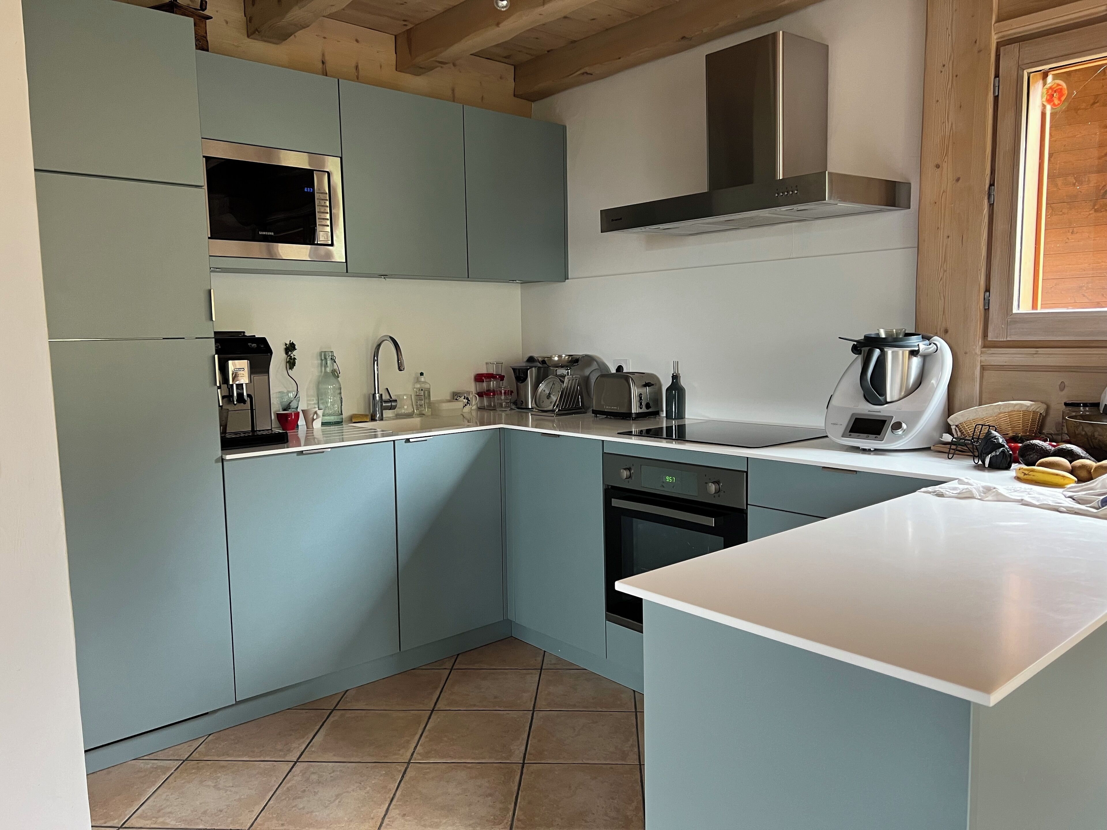 Une cuisine moderne avec des meubles de couleur bleu clair, un four à micro-ondes en acier inoxydable, un four encastré et une machine à café.