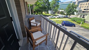 A balcony with wooden chairs and a table, overlooking a parking area and buildings. - Nebula on Medical Mile Cozy Cert (Grand Rapids)