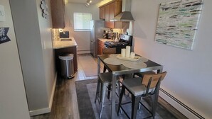 A compact kitchen with a dining area, a ceiling fan, and a small trash bin. - Nebula on Medical Mile Cozy Cert (Grand Rapids)