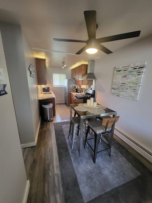 A compact kitchen with a dining area, a ceiling fan, and a small trash bin. - Nebula on Medical Mile Cozy Cert (Grand Rapids)