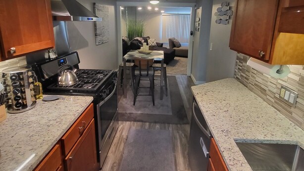 A kitchen with granite countertops, wooden cabinets, a stove, and a dining area with a table and chairs. - Nebula on Medical Mile Cozy Cert (Grand Rapids)