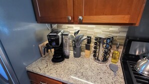 A compact kitchen with wooden cabinets, a granite countertop, a coffee maker, a blender, and a stove. - Nebula on Medical Mile Cozy Cert (Grand Rapids)
