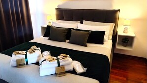 A neatly made bed with pillows, a bedside table with a lamp, a small plant, and a painting of a sunset on the wall.
