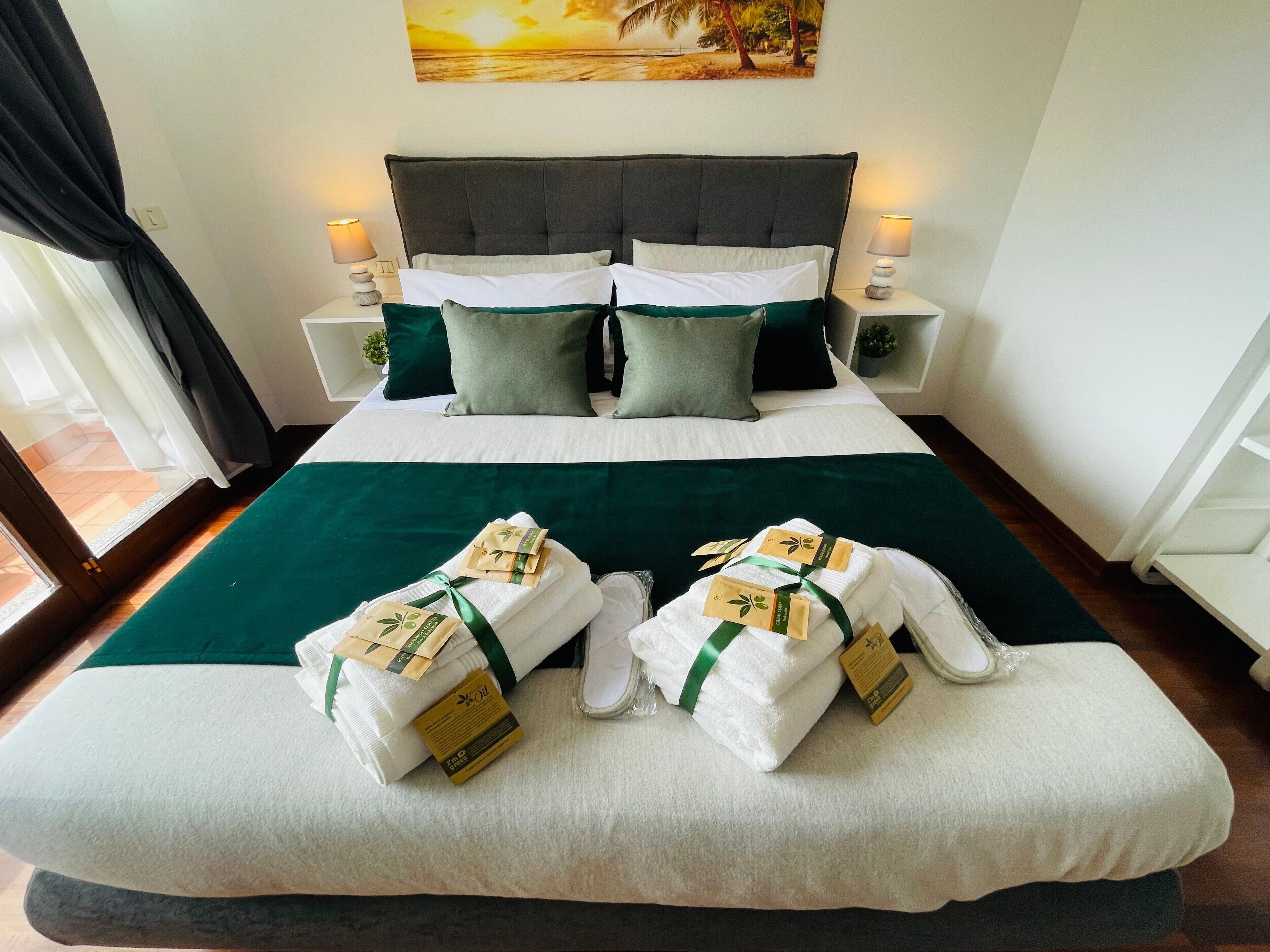 Una cama bien hecha con una colcha verde, dos almohadas y dos toallas con etiquetas.
