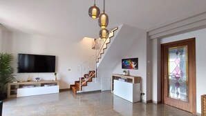 A modern living room with a staircase, a flat-screen TV, and a decorative wall piece.