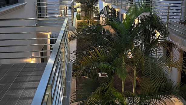 Un immeuble résidentiel à plusieurs étages, doté de balcons, d’escaliers et d’une cour intérieure agrémentée de palmiers.