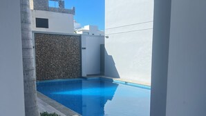 Un espace piscine extérieur moderne, doté d’une piscine à l’eau d’un bleu limpide, d’un mur en pierre et d’une terrasse en bois.