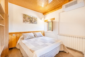 A bedroom with a wooden ceiling, a bed with a white bedspread, a painting on the wall, and a window. - Holiday Home 'Cal Sicull' with Mountain View, Private Pool and Wi-Fi (Santa Maria De Merles)