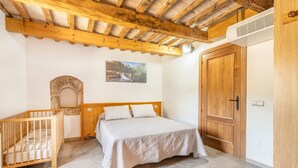 Un dormitorio con techo de madera, cama, cuna, armario y un arco de piedra.
