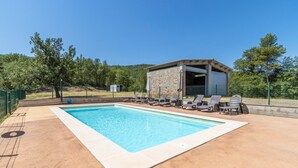 Una piscina con sillas de descanso, un edificio de piedra y un área cercada con árboles.