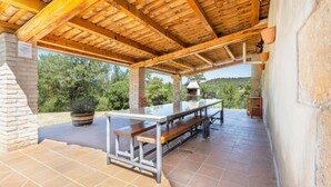 Un patio al aire libre con una pérgola de madera, una parrilla y una mesa larga para comer.