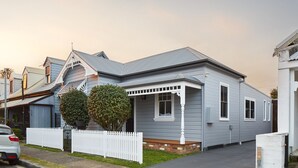A two-story house with a grey exterior, a white picket fence, and a small front porch. - Austin Cottage - Pet friendly holiday house in Newcastle (The Junction)
