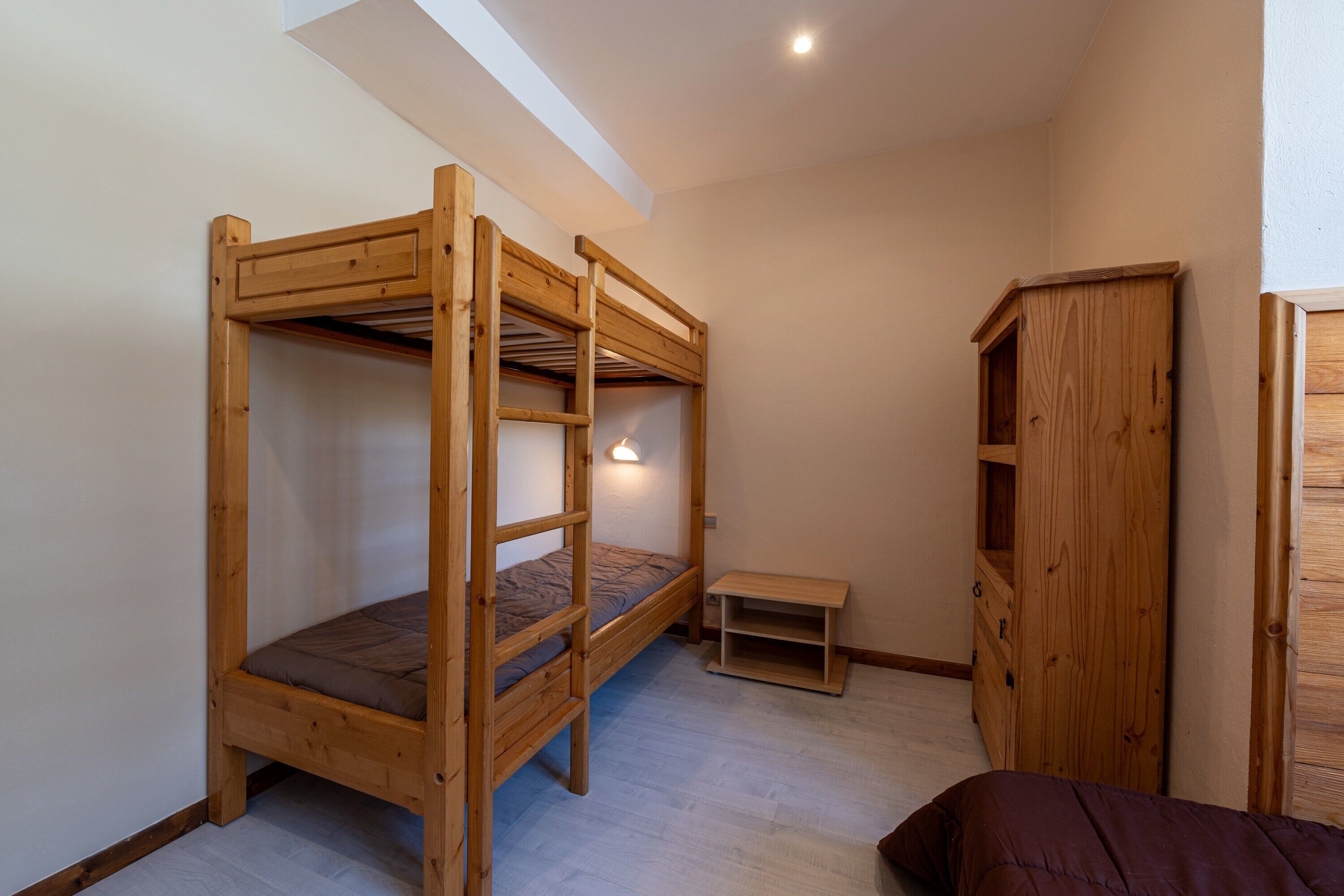 Una habitación con una cama litera, un armario de madera y un pequeño banco.