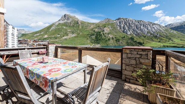 A terrace with a table and chairs, a stone wall, and a view of mountains. - Apartment 'Shamrock 2B' with Mountain View, Balcony and Wi-Fi (Tignes)