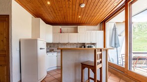A kitchen with wooden ceiling, white cabinets, a refrigerator, and a bar stool. - Apartment 'Shamrock 2B' with Mountain View, Balcony and Wi-Fi (Tignes)