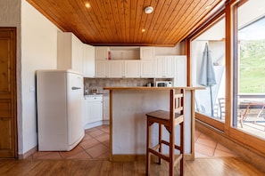 Una cucina con soffitto in legno, mobili bianchi, un frigorifero e uno sgabello da bar.
