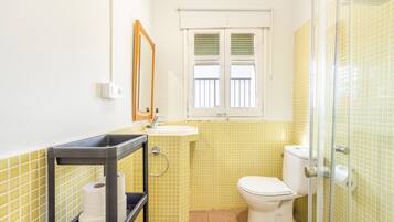 A bathroom with yellow tiled walls, a white toilet, a sink with a mirror above it, and a window with blinds.