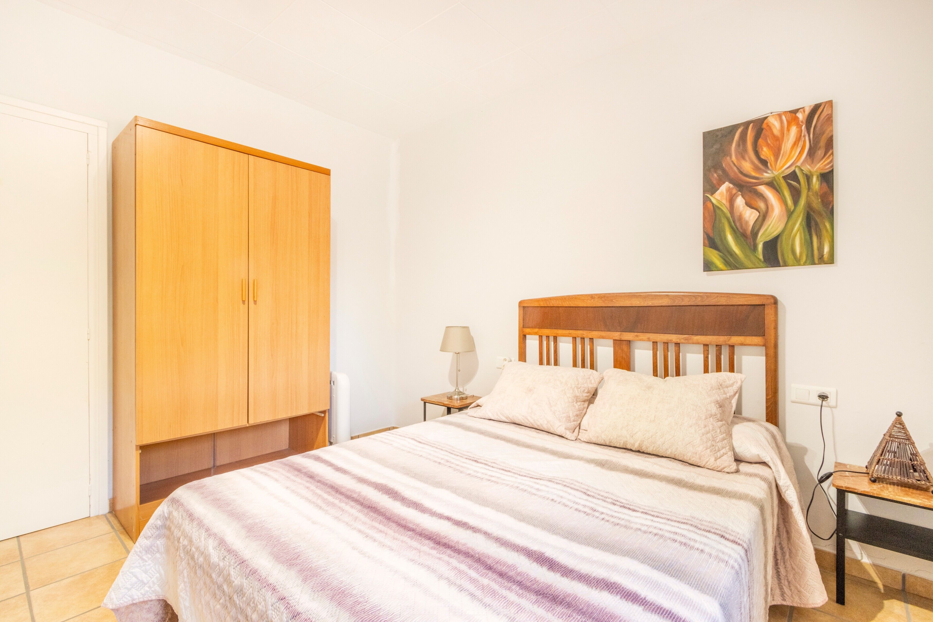 Een slaapkamer met een bed, een houten garderobe, een bedlamp en een schilderij aan de muur.